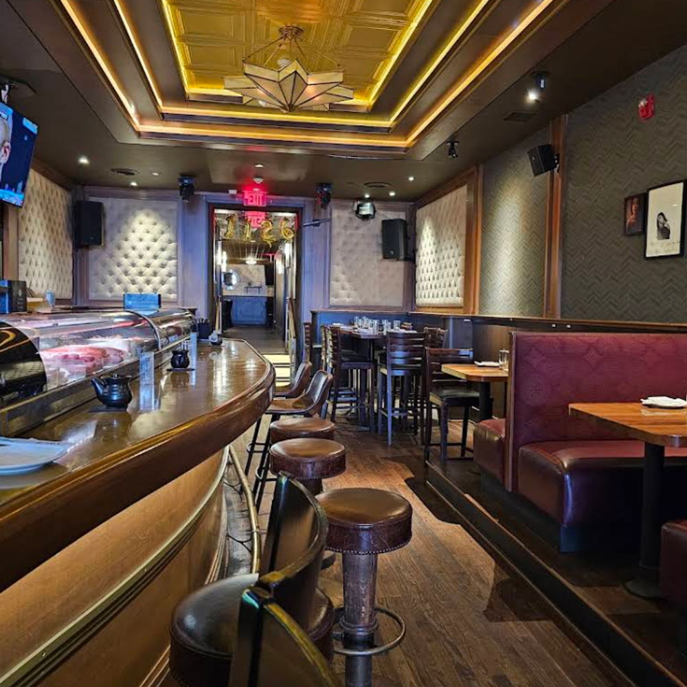 The-1126-Restaurant-Sushi-Restaurant-Columbus Upscale restaurant interior featuring a curved sushi bar, plush red booths, tufted walls, and a decorative ceiling with warm lighting.